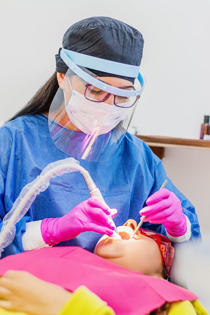 hero-img-02 A female dentist wearing protective gear performs a dental procedure on a patient in a clinic setting.